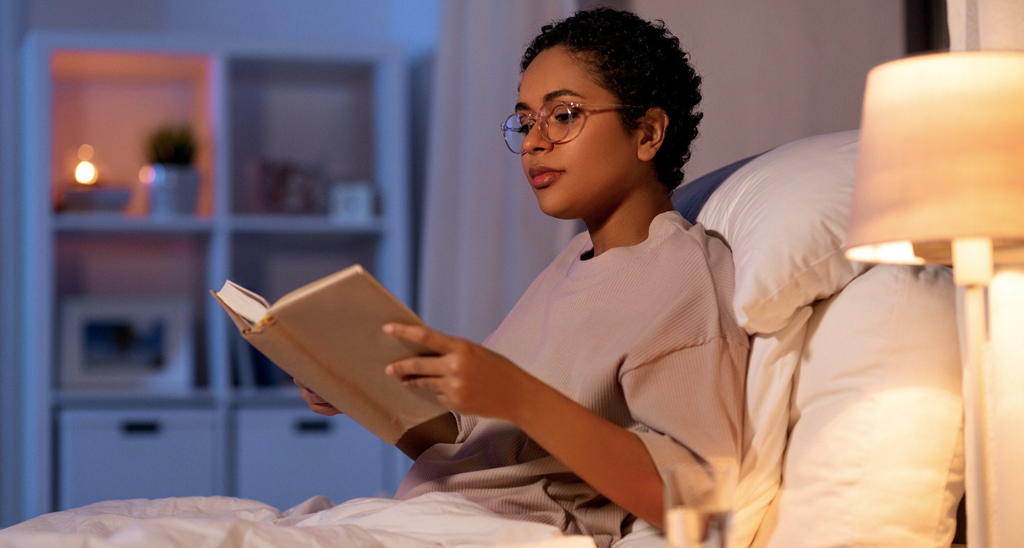 person wearing glasses and reading a book in dimly lit room