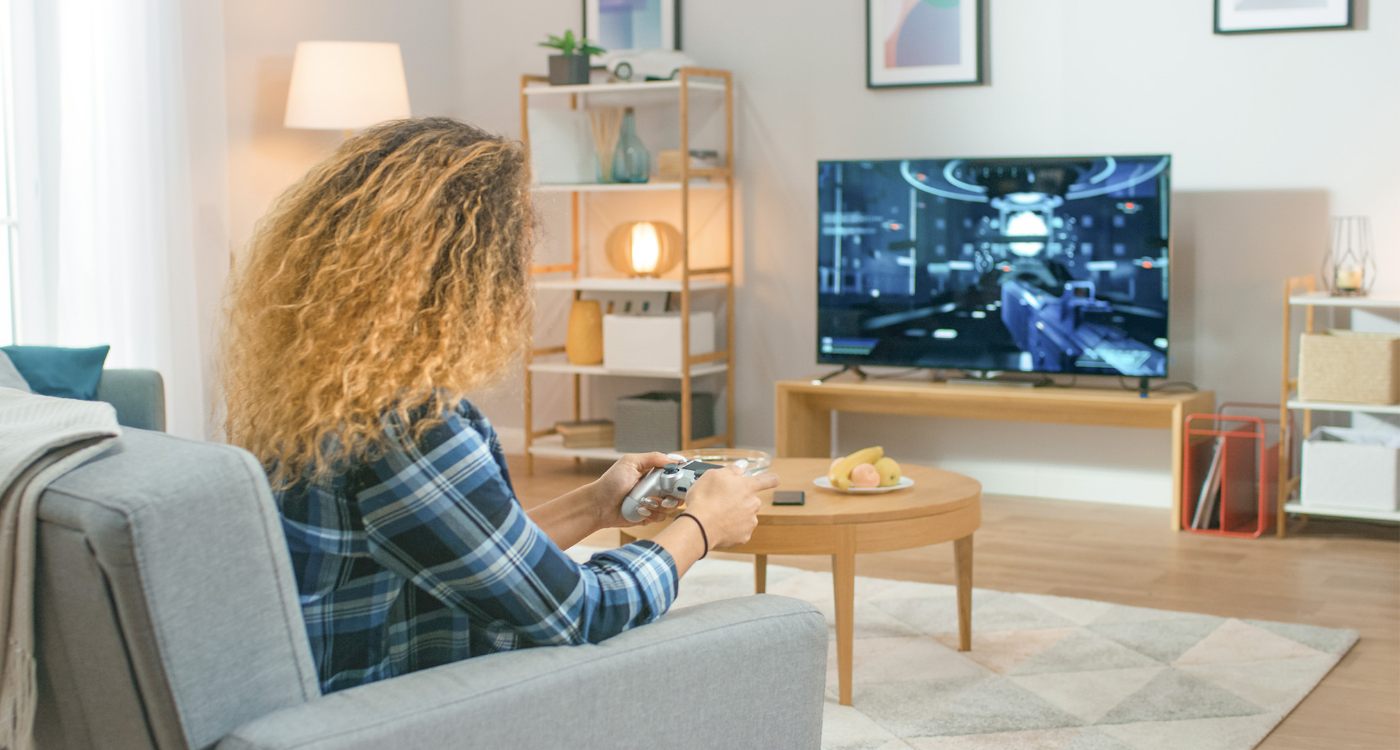 person with long curly hair in living room playing video games on a television