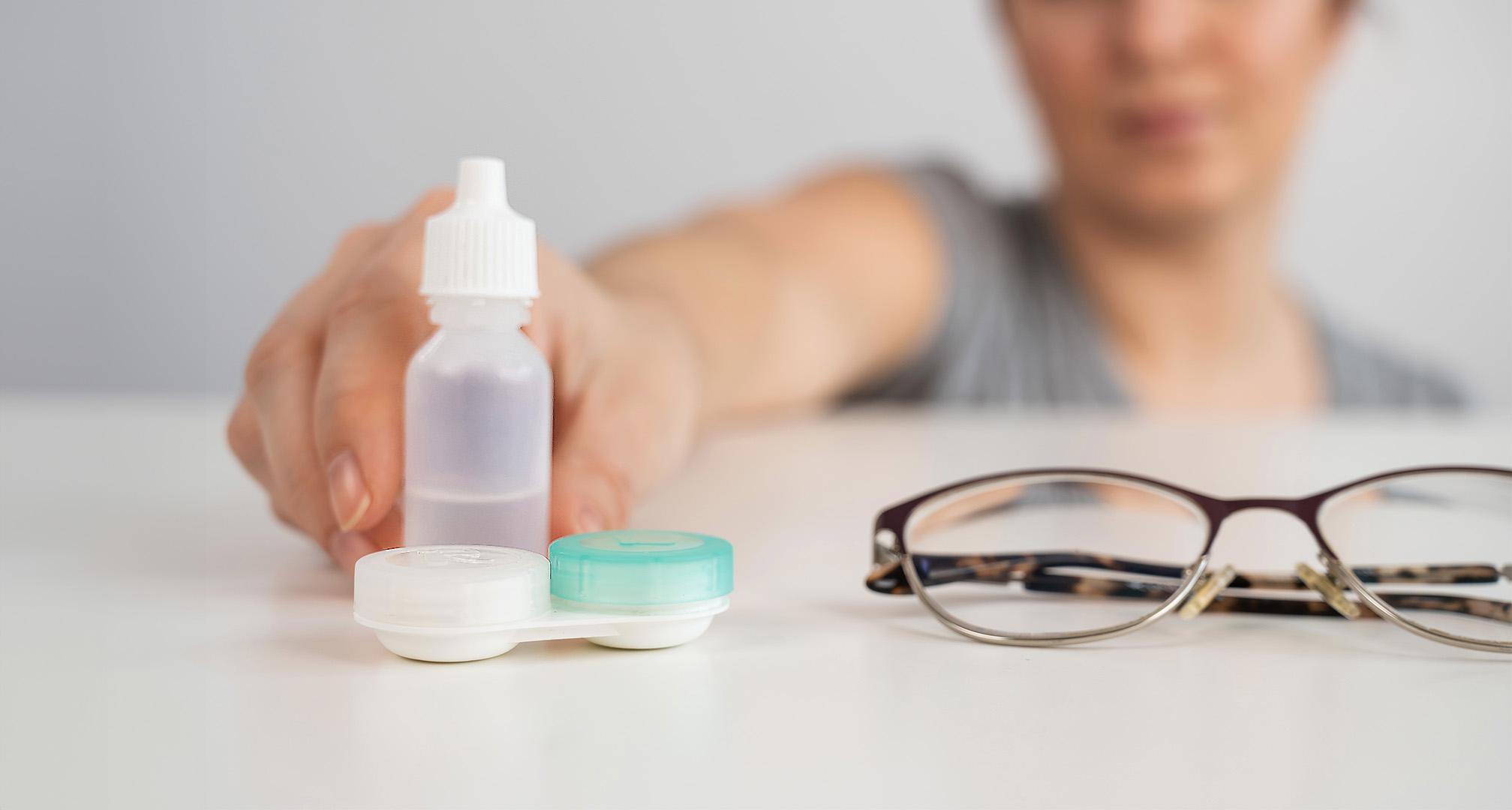 close up image of eye drops, contact lense case, and glasses on white table