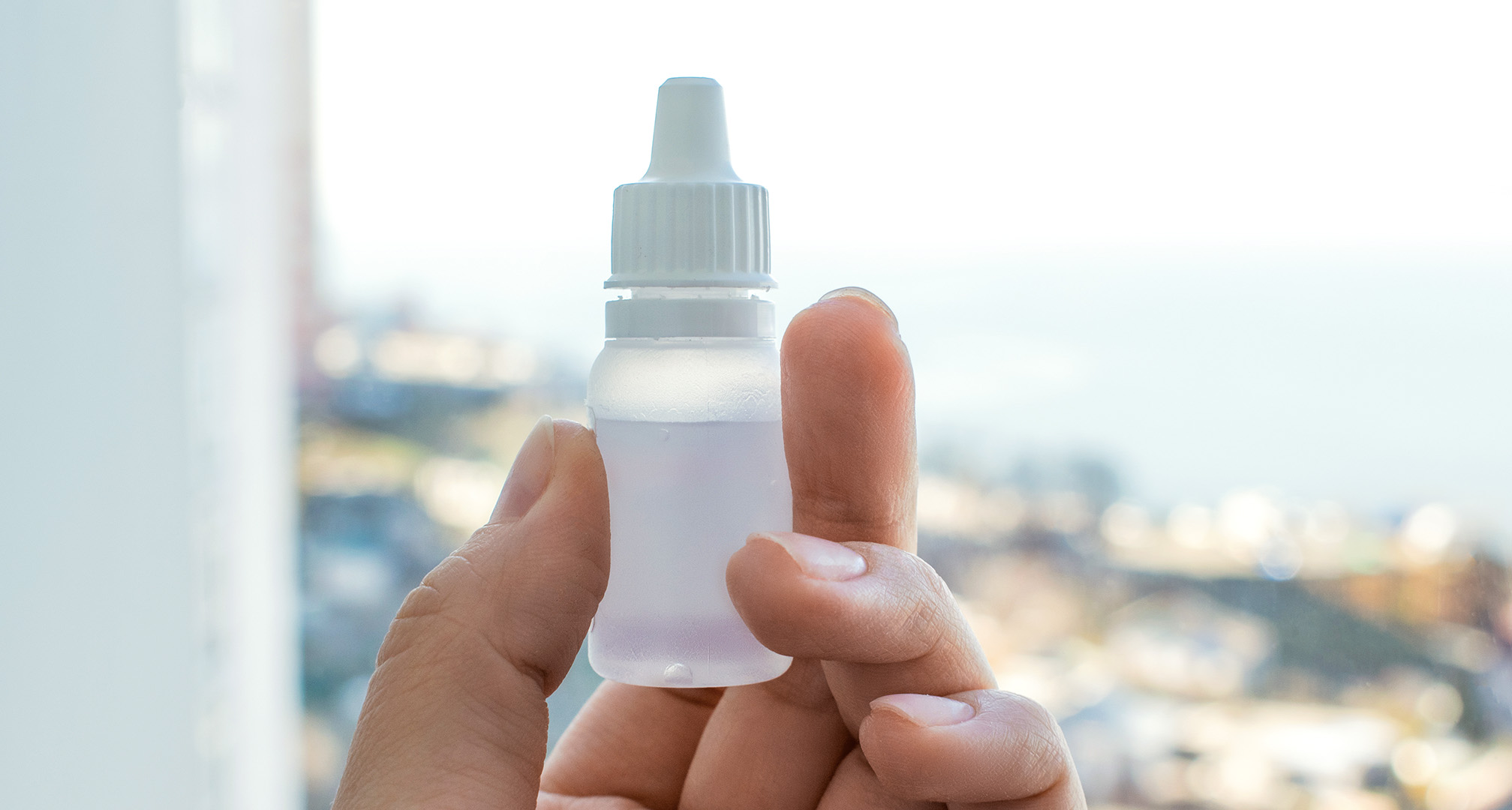 close up image of plain eye drops bottle in front of window
