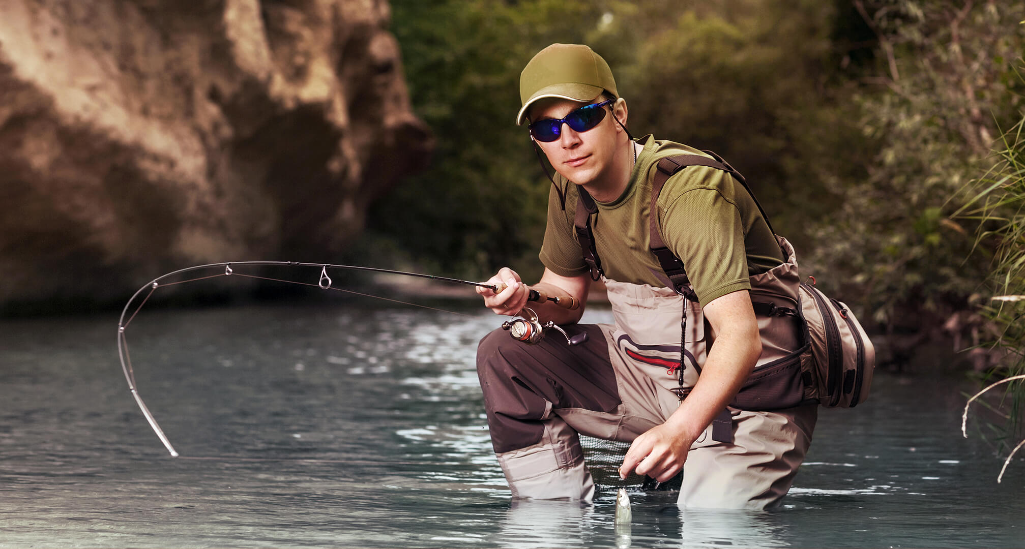 fisherman kneeling in water while wearing sunglasses